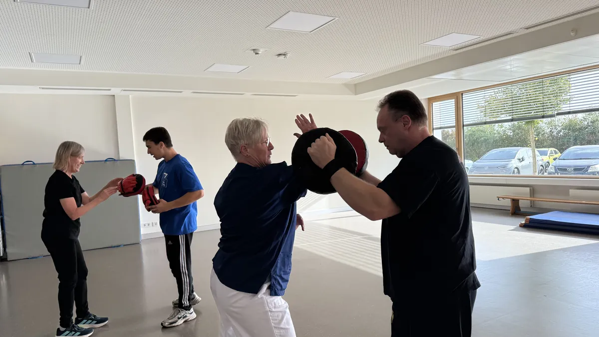 Mehrere Mitarbeitende der Klinik trainieren paarweise mit Handpratzen im Firmenkurs